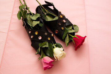 Three roses in black sandals decorated with crystals on a pink background. Women's comfortable shoes and flowers