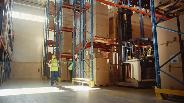 Retail Warehouse full of Shelves with Goods: Electric Forklift Truck Operator Lowers Pallet with Cardboard Box From a Shelf. People Working, Scanning Products, Using Trucks in Distribution Center