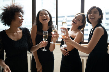 Overjoyed pretty positive young diverse ladies in classy black dresses having fun, celebrating birthday, toasting congratulating clinking glasses with champagne or white wine, enjoying party time.