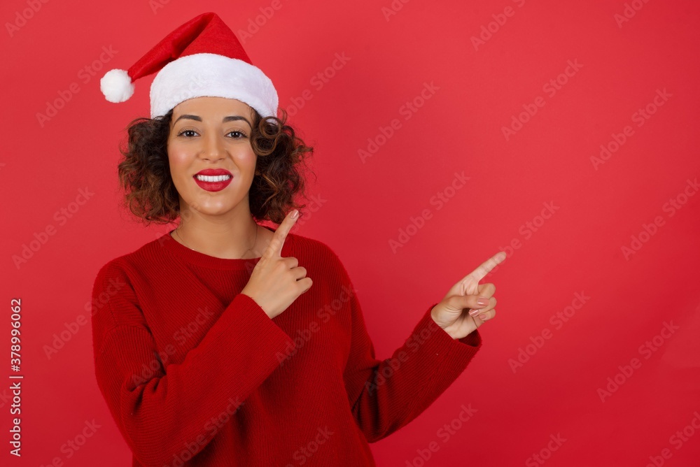 Wall mural Advertisement concept. Positive, pretty, caucasion woman with beaming smile in jeans shirt on grey background is pointing with her two index finger and looking on empty copy space.