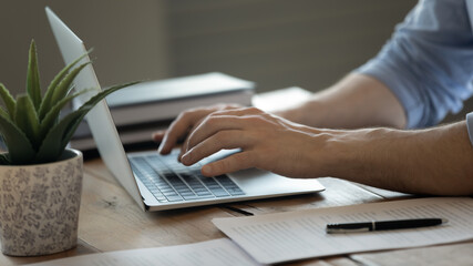 Crop close up of Caucasian man sit at desk texting typing on modern laptop keyboard. Businessman or male employee work on computer at home office workplace, consult client customer online on web.