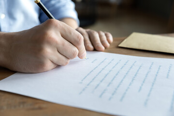 Crop close up of male sit at desk writing paper letter closing deal at workplace. Caucasian man...