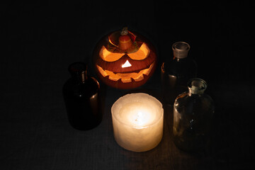Carved pumpkin lantern with candle and chemical bottles on gray linen cloth