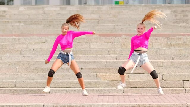 Two beautiful young girls in short shorts dancing free style street dancing, hip hop choreography on a huge stone staircase. Slow motion