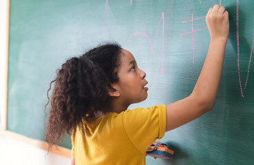 Afro american student girl writing on green chalkboard. Education, elementary school, learning, School children education concept.