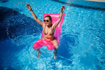 Sexy woman in sunglasses resting and sunbathing on a pink mattress in the pool. Young woman in...