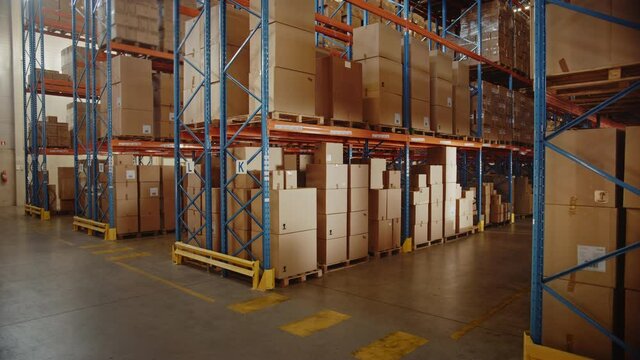 Large Retail Warehouse full of Shelves with Goods in Cardboard Boxes and Packages. Logistics, Sorting and Distribution Facility for further Product Delivery. Elevating Semi Side Camera View