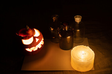 Carved pumpkin lantern with candle, chemical bottles and sheet of paper on gray linen cloth.
