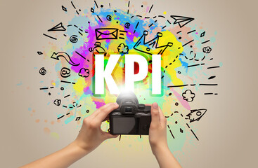 Close-up of a hand holding digital camera with abstract drawing and KPI inscription