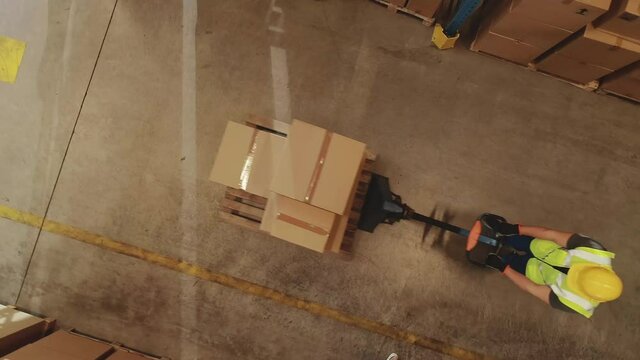 Top-Down Elevating View: Worker Moves Cardboard Boxes using Hand Pallet Truck, Walking between Rows of Shelves with Goods in Retail Warehouse