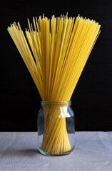 Dry spaghetti in a glass jar are on the table like a bouquet. Dark background. Vertical photography. Unusual use of food theme.