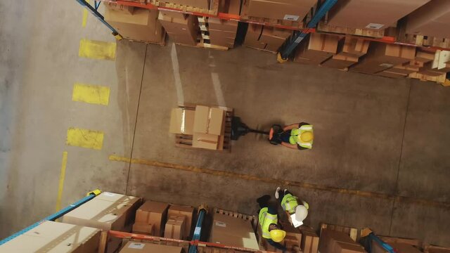 Top-Down Elevating View: Worker Moves Cardboard Boxes using Hand Pallet Truck, Walking between Rows of Shelves with Goods in Retail Warehouse