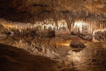 Cavern with stalactites and stalagmites with some light and dark areas. Also featured is a reflection of stalactites from above