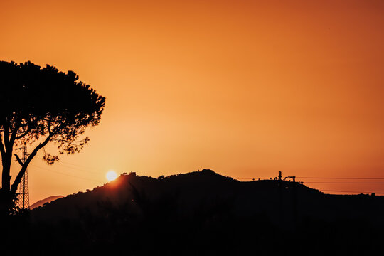 Mountains and tree silhouettes on a beautiful sunset with orange sky and sun going above the mountain