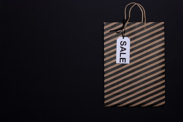 Paper craft bag with black stripes and sale tag on black background. Black Friday concept. Copy space, top view