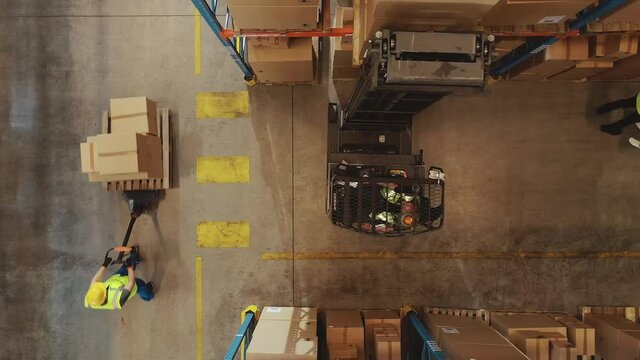 Top-Down Aerial Drone Shot: Electric Forklift Truck Operator Lifts Pallet with Cardboard Box of in a Big Retail Warehouse a Shelf. Logistics Product and Goods Delivery and Distribution Center