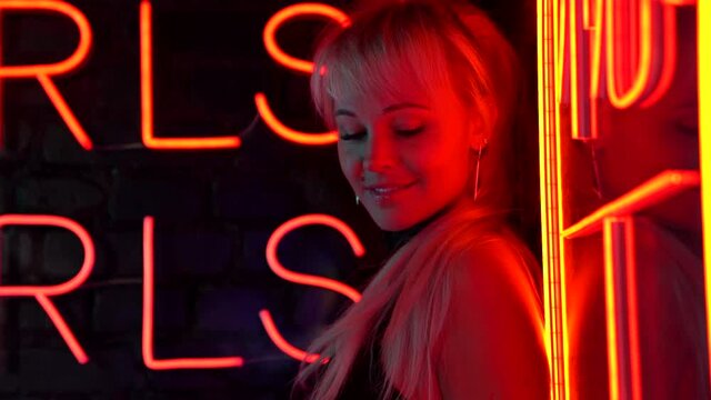 young sexy prostitute is waiting clients on street at night, flirting with camera, neon lights