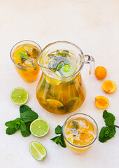 Apricot cocktail or ice tea with fresh mint, lime and apricots. Summer refreshing cold drink. Light concrete background.