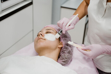 Obraz na płótnie Canvas Professional Esthetician Apply Face Mask to the client's face in spa beauty center. Young woman getting facial care by beautician at spa salon Acne Treatment, face peeling mask