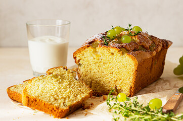 Delicious homemade grape loaf cake with thyme and sugar powder on parchment paper. Light stone background.