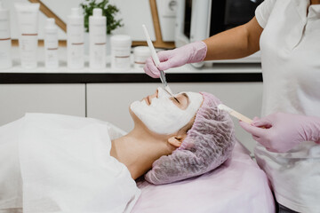 Obraz na płótnie Canvas Cosmetologist applying mask on client's face in spa salon. Young woman getting facial care by beautician at spa salon Acne Treatment, face peeling mask, spa beauty treatment, skincare