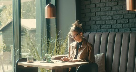 Woman working on tablet, sitting in cafe with cup of coffee. Girl in glasses pauses after work. Online chat with friends, long distance communication. Staying connected. 4K video