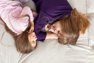 Little girl spends time playing with mom while lying in bed