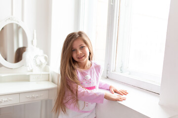 Portrait of a beautiful teenage girl stands by the white window