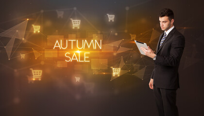 Businessman with shopping cart icons and AUTUMN SALE inscription, online shopping concept
