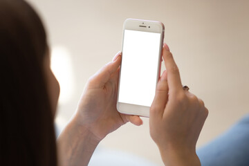 Close up of Young woman using smartphone with empty white mock up screen left for copy space. Client visiting website of company, chatting or reading ads on cellphone. View over the shoulder