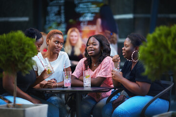 Happy African American Women, friends sitting together at the outdoor restaurant at summer day