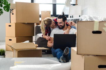 Fototapeta premium Young couple moving in new home.Sitting on floor and relaxing after unpacking.Looking something on laptop