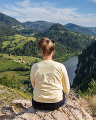 Naklejka premium Young girl in the nature. Back view portrait of a single woman watching the Spajici lake from the height in west Serbia