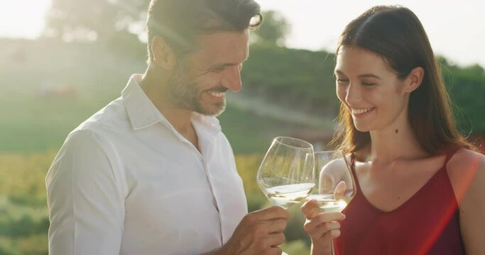 Authentic shot of happy couple in love is enjoying romantic date and cheering with white wine glasses to celebrate their anniversary and timeless love on scenic vineyards background.