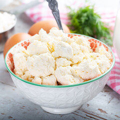 Curd cheese or cottage cheese in white bowl with glass of milk on wooden table, closeup view.