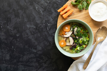 Soup with fresh white mushrooms and potato - traditional dish of russian cuisine in a clay bowl over dark wooden background.Top view with copy space.
