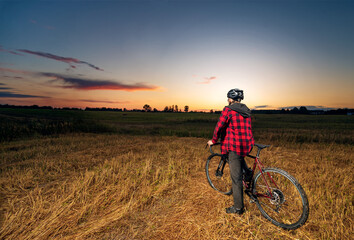 Fototapeta na wymiar Rear view of a cyclist on a gravel bike in a field at sunset. Active cycling concept.