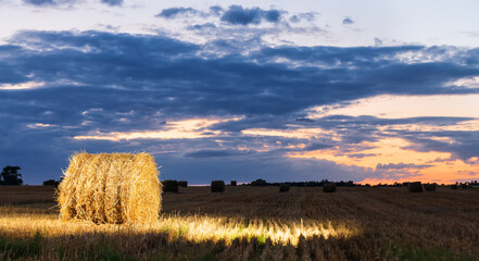 Evening landscape of haystacks in the field. The stack is illuminated by a flash.