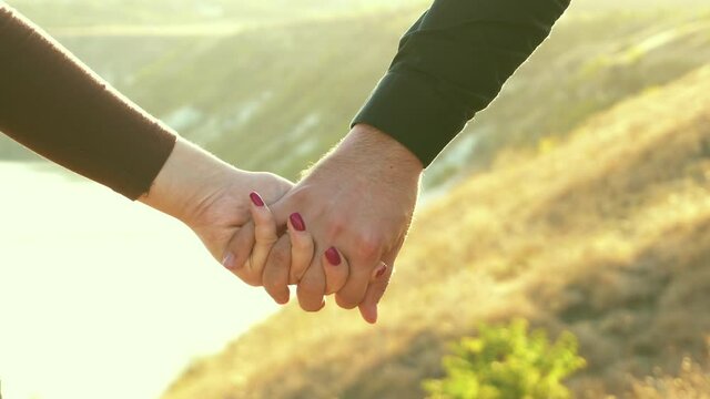 close up footage of couple holding hands outdoor in field during sunset