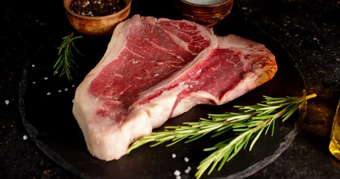 Steak raw beef t-bone on a stone board with spices.