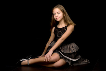 Fototapeta na wymiar A little girl is sitting in the studio on the floor on a black background.
