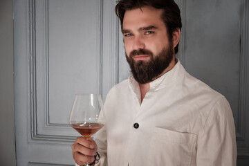Bearded handsome man dressed in white shirt holds a glass of cognac