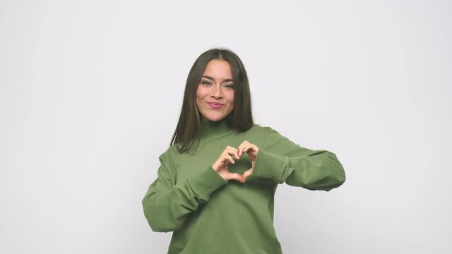 Young cute woman smiling and showing a heart shape with hands