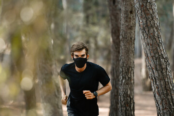 Fototapeta premium Joven atleta corre por el bosque con una mascarilla negra