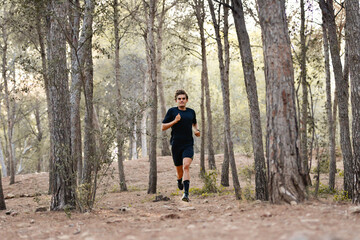 Atleta joven corriendo por un bosque, vestido con una camiseta negra y pantalón corto negro