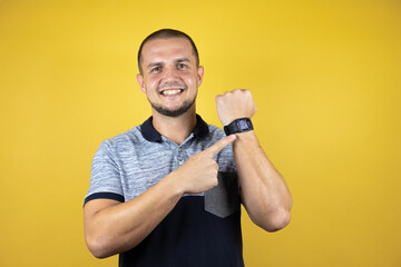Russian man standing over insolated yellow background surprised and pointing his watch because it's...