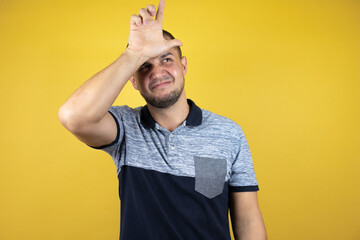 Russian man standing over insolated yellow background making fun of people with fingers on forehead...