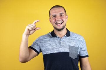 Russian man standing over insolated yellow background with hand doing small size sign with fingers looking and the camera.