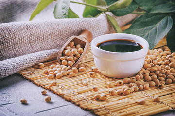 Soy sauce with soya beans scattered on a bamboo napkin against the background of burlap and branch...
