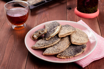 Traditional Russian sweet shortcrust pastry with quark or cottage cheese and raisins, sochni or sochniki pies or pirozhki with poppy seeds on pink plate with tea in the morning on brown wooden table
